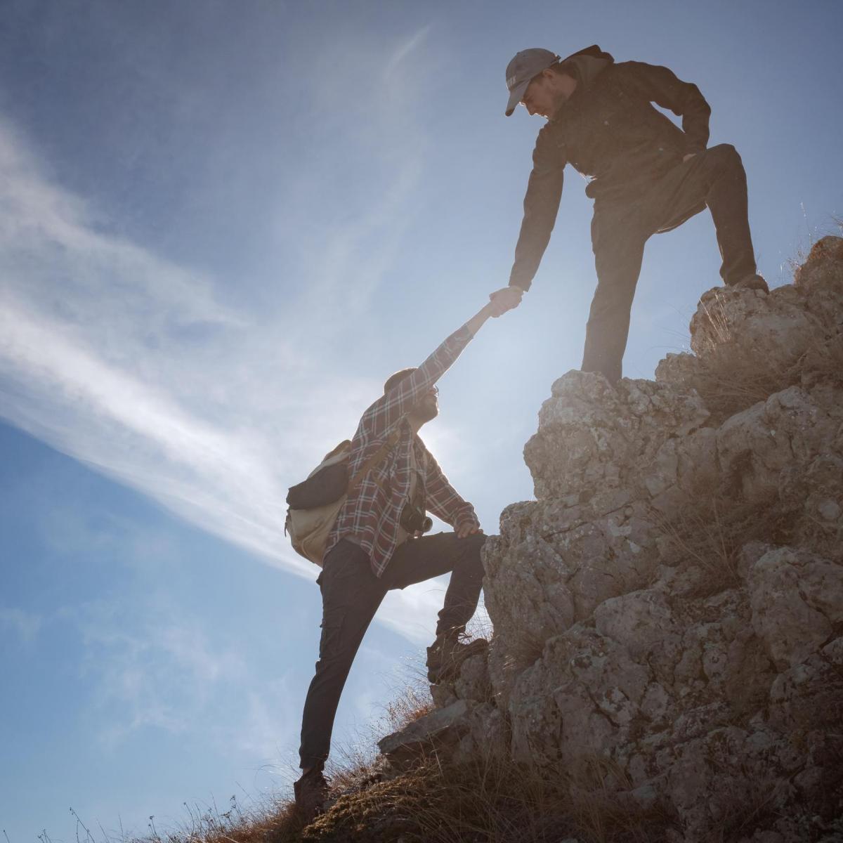 Help and assistance concept. Silhouettes of two people climbing mountains and helping against the blue sky. Walk in the clouds. Discovery Travel Direction Concept